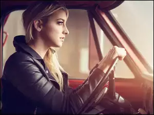 Zapatrzona blondynka z rękoma na kierownicy samochodu
