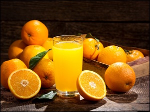 Szklanka soku pomarańczowego obok skrzynki z pomarańczami