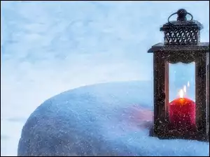 Latarenka z zapaloną świeczką na zaśnieżonym kamieniu