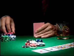 Dłonie mężczyzny z żetonami kartami do gry w pokera i szklanka whisky