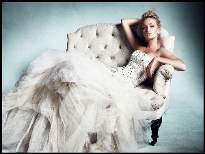Blondwłosa kobieta w pięknej białej sukni odpoczywa na kanapie