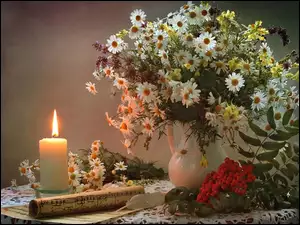 Kompozycja z kwiatów rumianku i zapalonej świecy