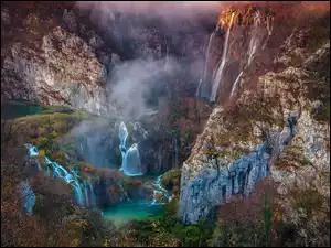 Wodospady na skałach w zamglonym Parku Narodowym Jezior Plitwickich w Chorwacji