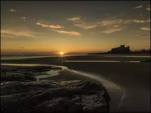 Zachód słońca nad plażą morza Północnego z angielskim zamkiem Bamburgh w oddali