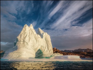 Góra lodowa na morzu z widokiem na odległe skały i góry