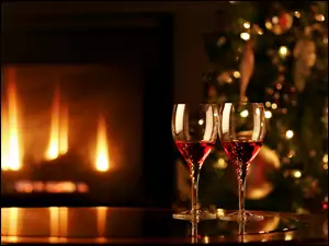 Dwie lampki wina obok świątecznej choinki w blasku kominka