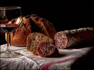 Chleb i kiełbasa położona na ściereczce obok kieliszka z winem