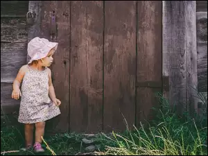 Zapatrzona dziewczynka oparta o drewnianą ścianę