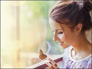 Kobieta przy oknie obserwuje frunącego motyla