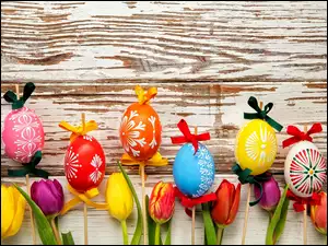 Wielkanocne kolorowe pisanki na patyczkach obok tulipanów