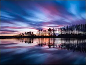 Drzewa i niebo w lustrzanym odbiciu jeziora o zachodzie słońca