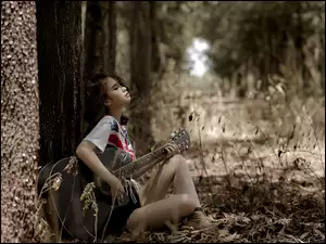 Dziewczyna z gitarą siedzi pod drzewem