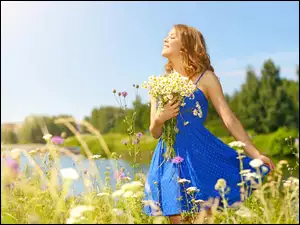Dziewczyna w niebieskiej sukience pośród kwiatów na łące