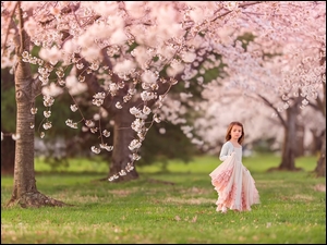 Dziewczynka w różowej sukience między kwitnącymi drzewami