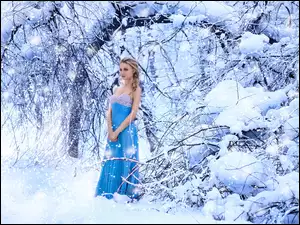 Blondynka w niebieskiej sukience pozuje w zimowym lesie