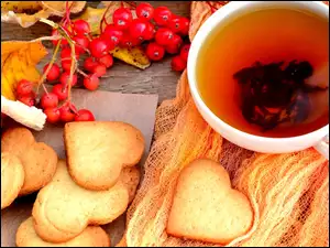 filiżanka herbaty z piernikowymi serduszkami na stole jesienną jarzębiną