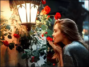 Kobieta wąchająca kwiatki pod latarnią