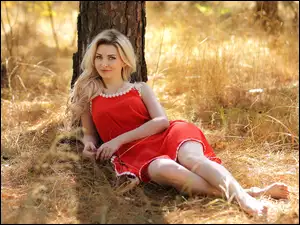 Uśmiechnięta Blondynka w czerwonej sukience pod drzewem