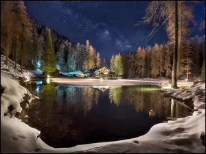 Gwiezdna noc nad zimowym lasem jeziorem i domami