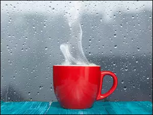 Kubek czerwony z kawą pod oknem z kroplami deszczu