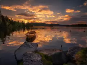 Zachód słońca nad leśnym kamiennym jeziorem z łódka