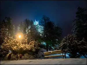 Zimowy park z ławką z widokiem na oświetlony zamek