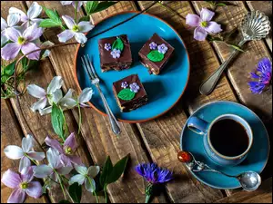 Porozrzucane polne kwiaty obok filiżanki z kawą i kawałków ciasta