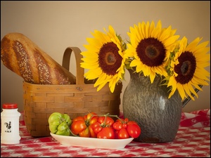 Chleb w koszyku obok pomidorów i solniczki ze słonecznikami w dzbanku