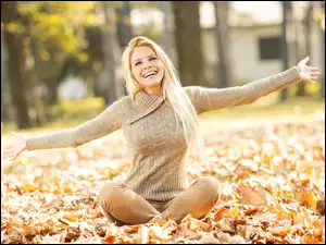 Radosna dziewczyna siedzi na jesiennych liściach