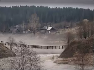 Mglista leśna rzeka z mostem i domami
