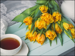 Bukiet żółtych tulipanów obok filiżanki z herbatą
