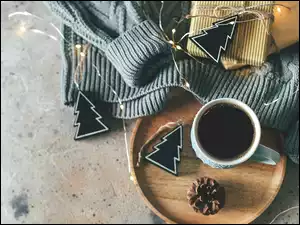 Świąteczna kawa na tacy obok swetra z prezentami