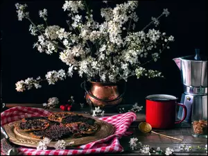 Wiązanka kwitnących gałązek obok lampy, kawy i talerza z ciastkami