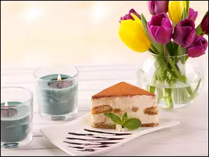 Tulipany w szklanym wazonie obok porcji ciasta i świeczek