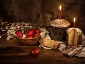 Bazie na koszyczku z pisankami i obok świątecznych babek ze świeczkami
