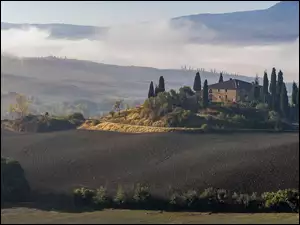 Dom wśród cyprysów na zamglonych wzgórzach Toskanii