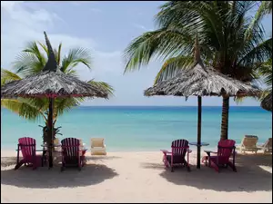 Leżaki pod parasolami i palmami na karaibskiej plaży