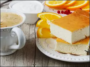 Dwa kawałki sernika pomarańczowego obok filiżanki kawy