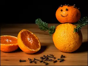 Pomarańczowy bałwanek obok połówek pomarańczy i goździków