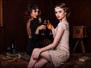 Dwie kobiet w wieczorowych sukniach trzymające lampki z winem