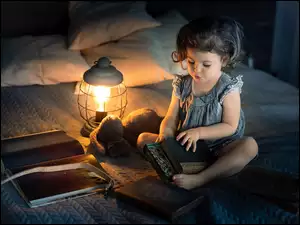 Dziewczynka z książkami na łóżku przy zapalonej lampce