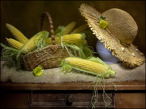 Słomiany kapelusz obok koszyka z kolbami kukurydzy