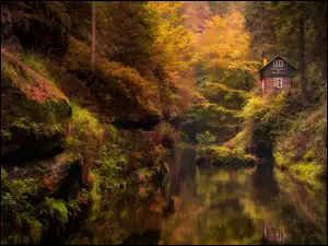 Dom na skałach nad leśną rzeką w jesiennej scenerii