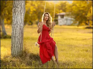 Kobieta w czerwonej sukni na huśtawce na drzewie