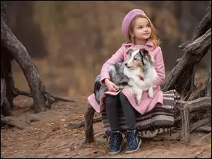 Dziewczynka w różowym płaszczu i berecie z owczarkiem szetlandzkim na kolanach