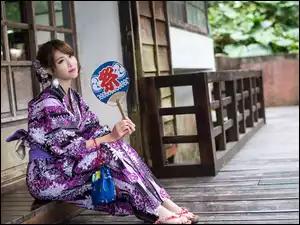 Azjatka w kimono z wachlarzem siedzi przed domem