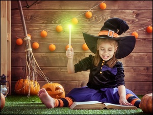 Dynie na Halloween ułożone obok dziewczynki z czarodziejską różdżką