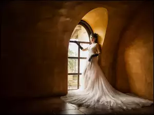 Dziewczyna w białej sukience stoi przy oknie