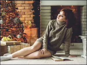 Zamyślona kobieta w swetrze przy kominku i świątecznej choince