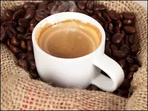 Filiżanka z kawą postawiona w worku na ziarnach kawy